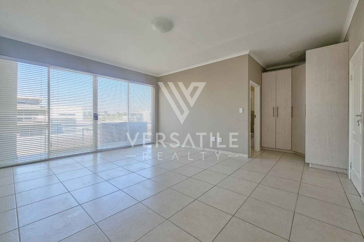 Spacious, light-filled bedroom featuring neutral tiled flooring, built-in cupboards, and large sliding glass doors with venetian blinds leading to an outdoor area.