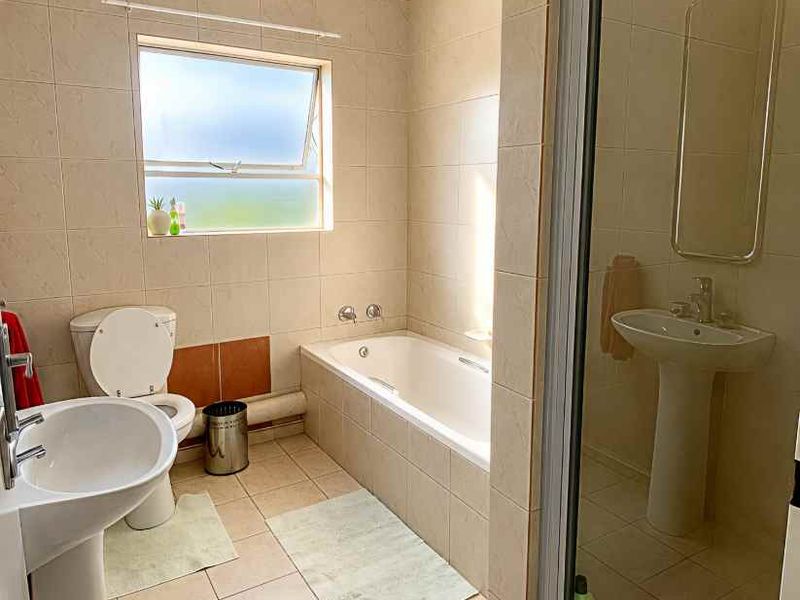 A functional bathroom featuring a pedestal basin, built-in bathtub, and separate shower enclosure with neutral ceramic tiling throughout.