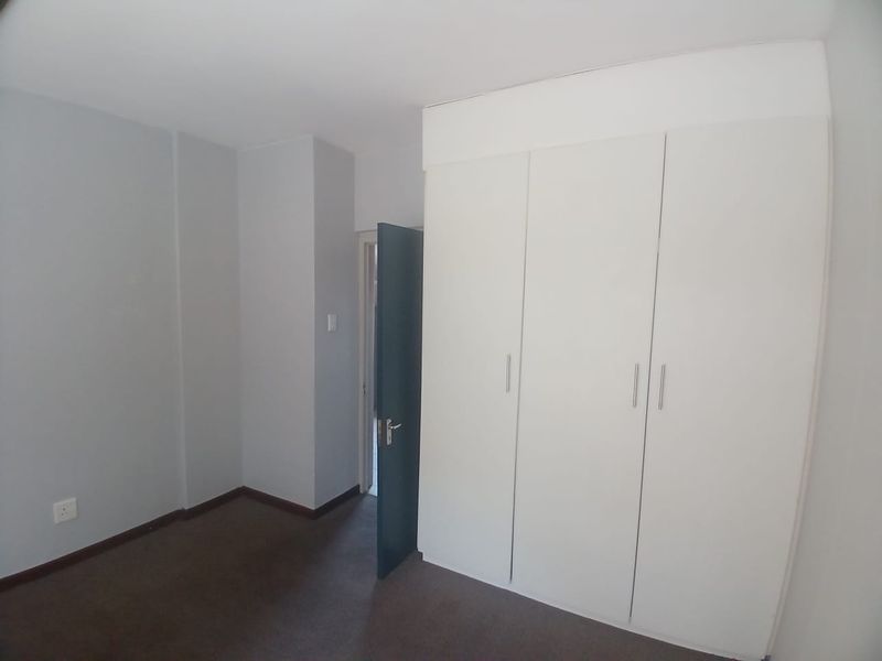 A clean, empty bedroom featuring neutral walls, carpeted flooring, and ample built-in cupboard storage space.