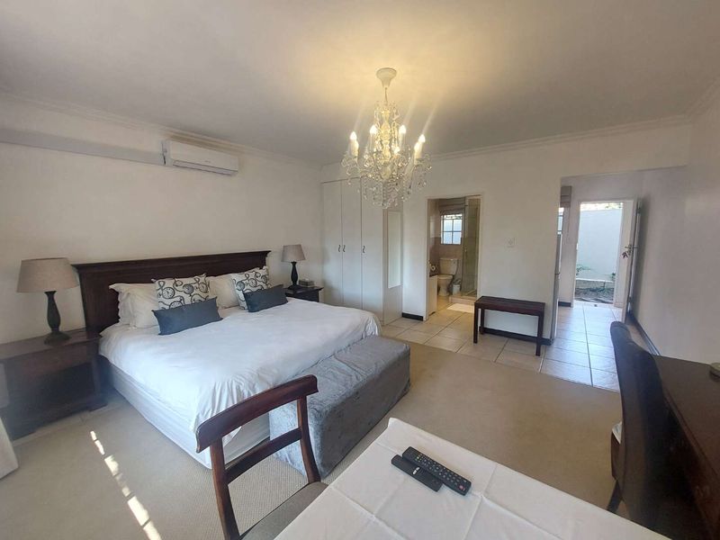 Spacious bedroom featuring built-in cupboards, a split-system air conditioner, and an en-suite bathroom with tiled flooring.
