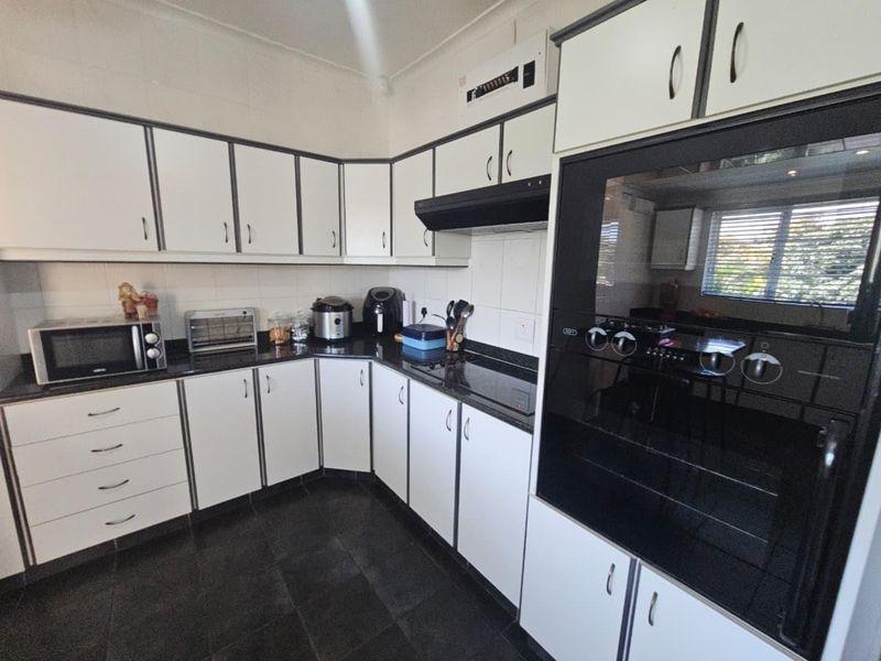 A functional kitchen featuring white cabinetry, dark countertops, a built-in oven, and a hob, with tiled flooring and backsplash throughout.