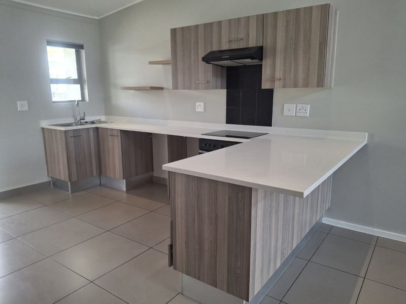 Modern kitchen featuring wood-finish cabinetry, stone countertops, an electric hob with extractor fan, and tiled flooring in an open-plan layout.