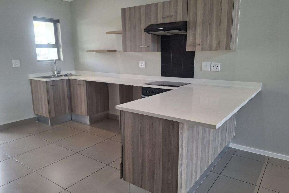 Modern kitchen featuring wood-finish cabinetry, stone countertops, an electric hob with extractor fan, and tiled flooring in an open-plan layout.