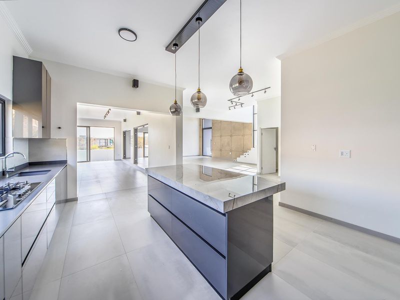 Modern open-plan kitchen featuring a central island with stone countertop, gas hob, sleek cabinetry, and contemporary pendant lighting, flowing into an expansive living area.