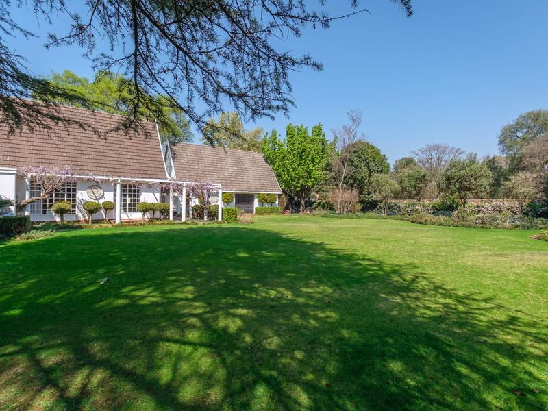 A spacious rear garden featuring a well-maintained lawn, mature trees, and a covered patio area attached to the main residence.