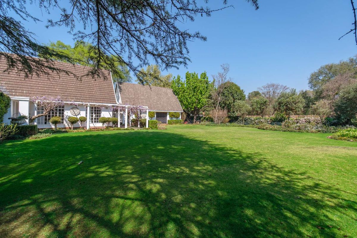 A spacious rear garden featuring a well-maintained lawn, mature trees, and a covered patio area attached to the main residence.
