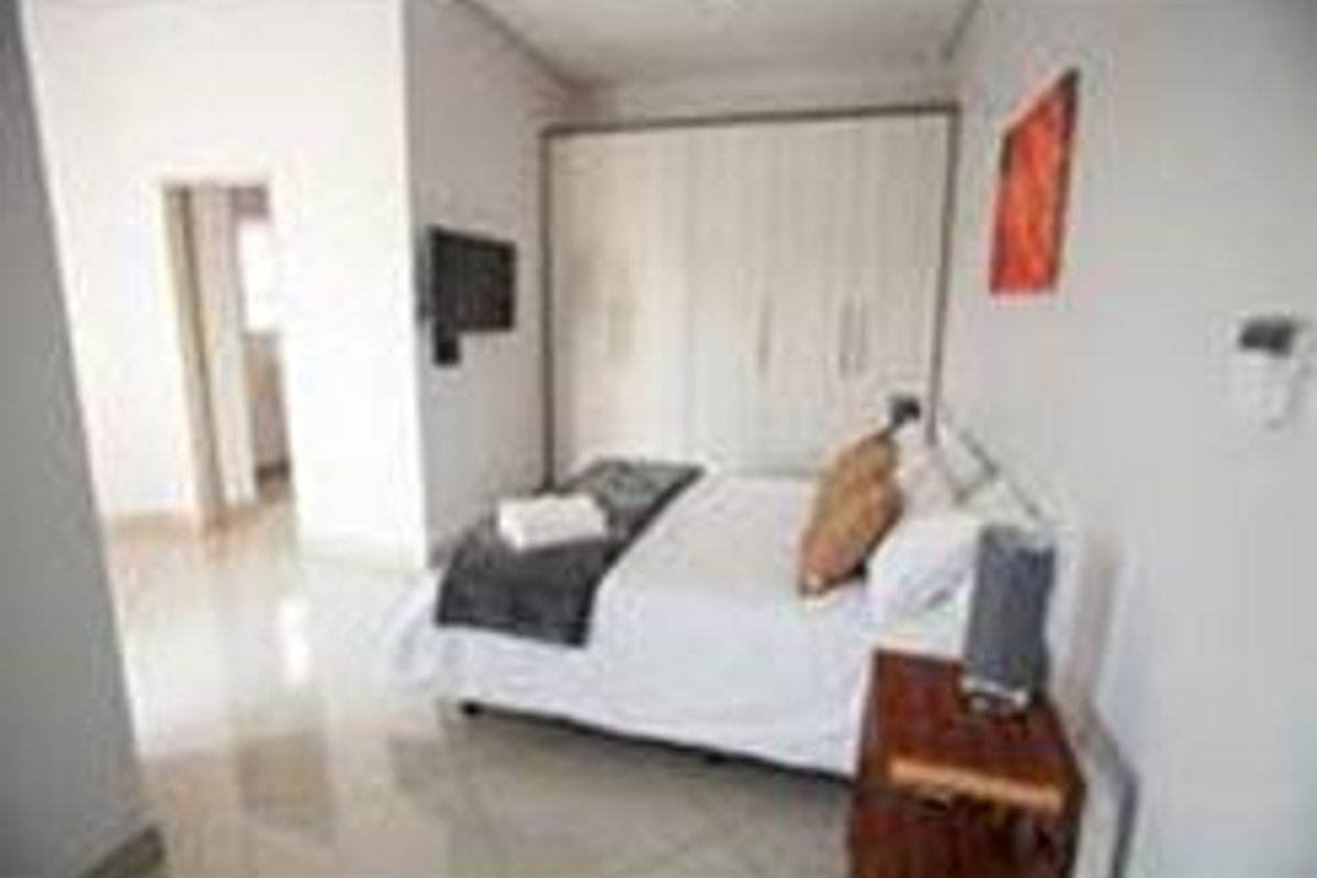 A well-lit bedroom featuring neutral tiled flooring and ample built-in cupboard storage space.