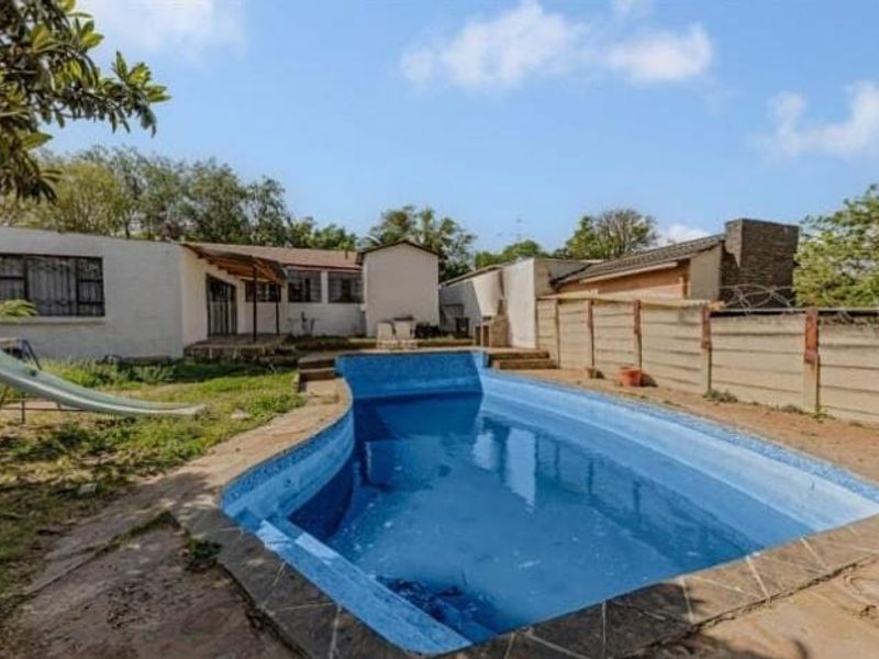 Rear garden area featuring a swimming pool, precast boundary walling, and direct access to the main dwelling structure.