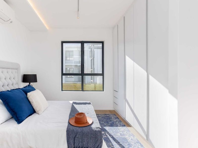 Modern bedroom featuring sleek floor-to-ceiling built-in cupboards, recessed lighting, and an air conditioning unit, finished with clean white walls and large window.