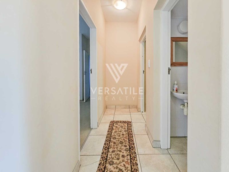 A clean, neutral hallway featuring tiled flooring and access to adjacent rooms, including a small wash area with a wall-mounted basin.