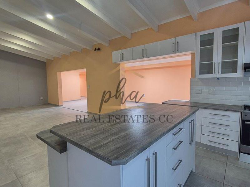 Spacious open-plan kitchen and living area featuring a central island, modern cabinetry, gas stove, and exposed beam ceilings with neutral tiled flooring.