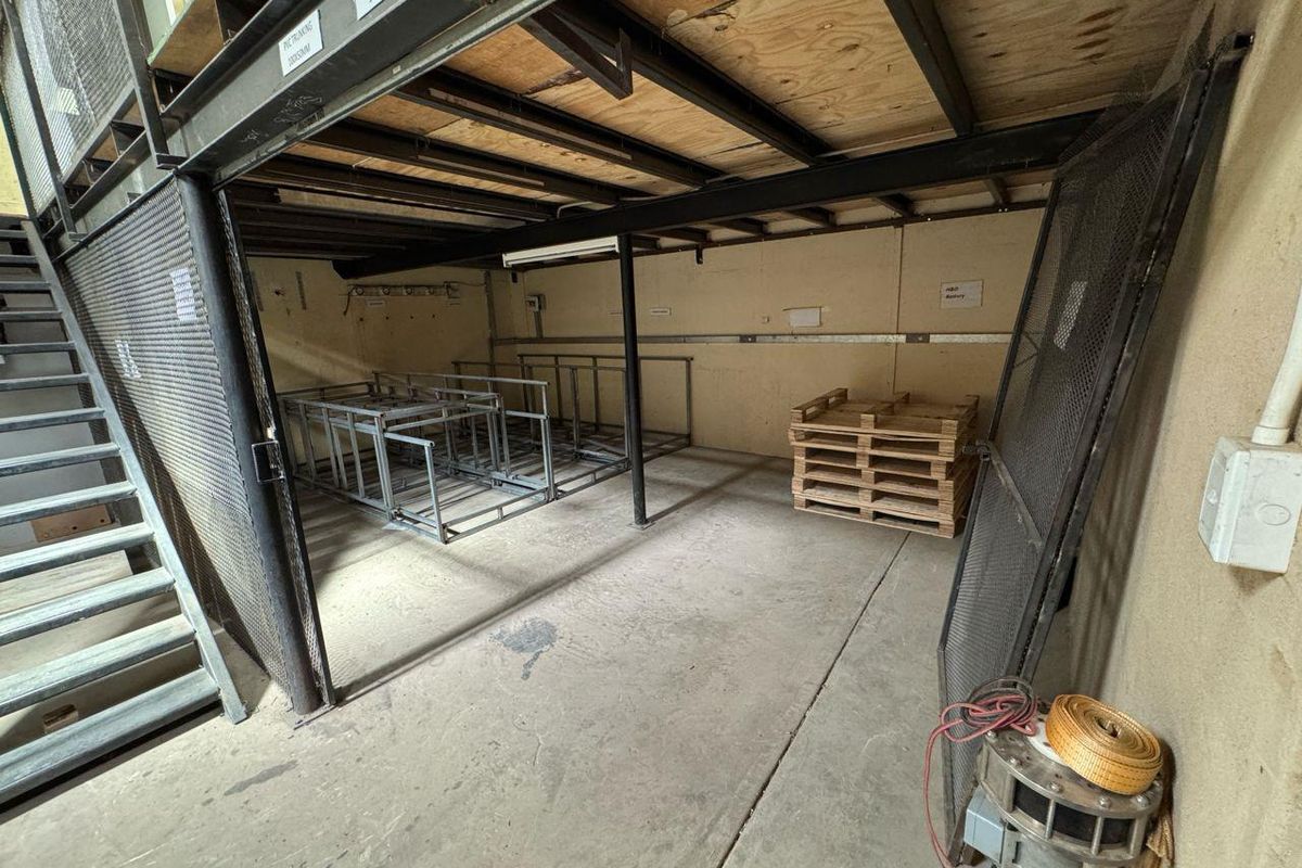 Industrial utility space featuring a mezzanine level, concrete flooring, and metal mesh partitioning, suitable for storage or workshop use.