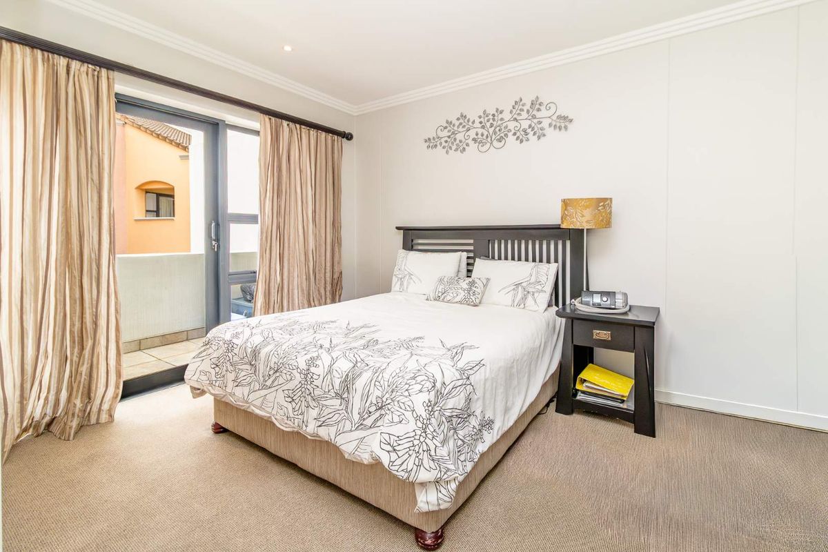 A well-maintained bedroom featuring neutral carpeting, crown molding, and a sliding glass door providing direct access to a private balcony.