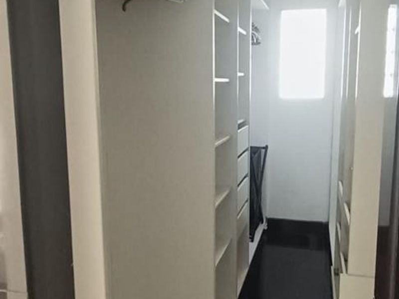 A walk-in closet featuring extensive built-in white cabinetry, shelving, and dark tiled flooring, providing ample storage space.