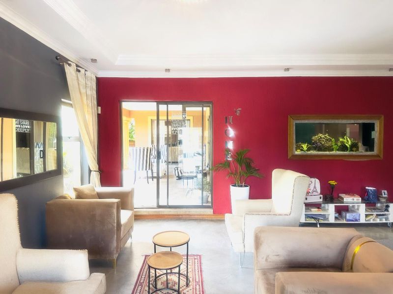 A living room featuring a bold red accent wall, recessed ceiling lighting, and sliding glass doors providing access to an outdoor patio area.