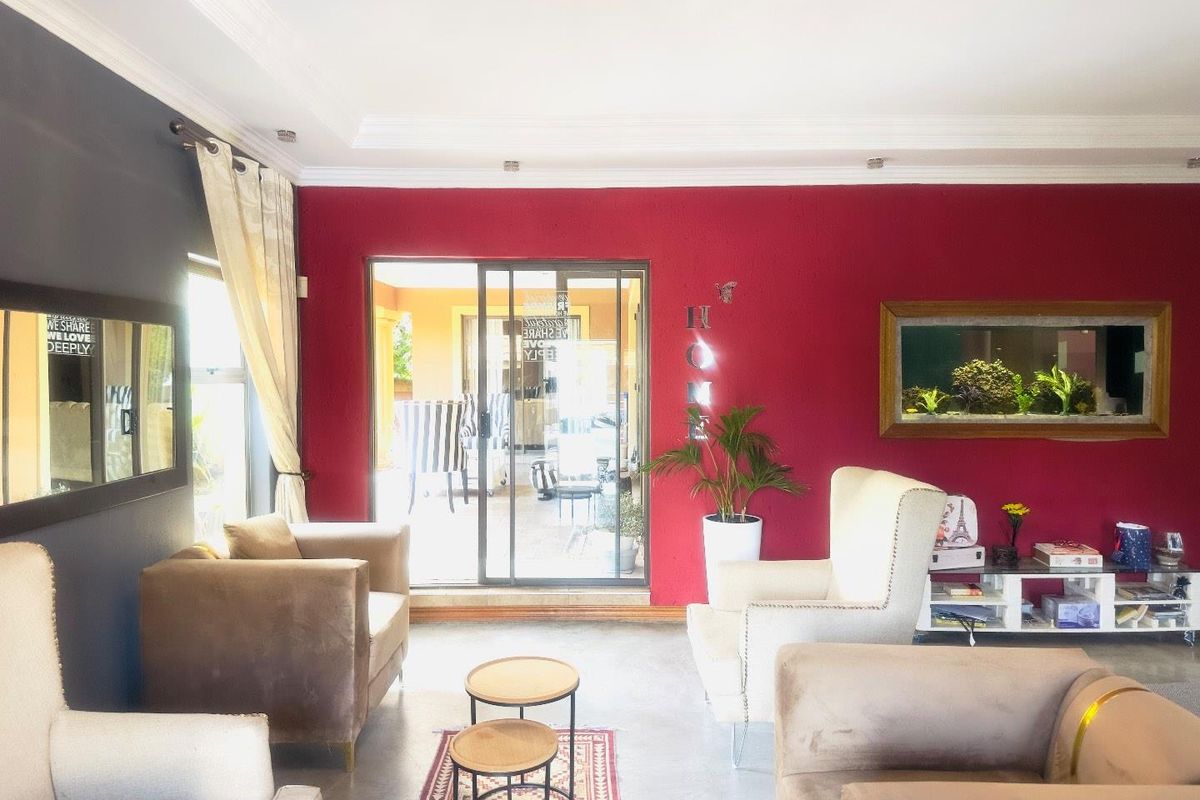 A living room featuring a bold red accent wall, recessed ceiling lighting, and sliding glass doors providing access to an outdoor patio area.