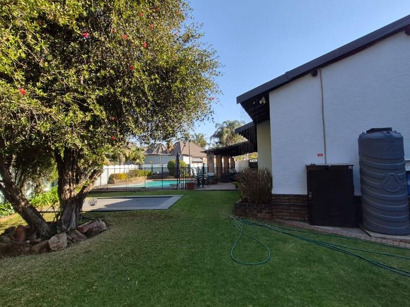 Rear garden view featuring a swimming pool, paved patio area, and installed water storage tanks against the side of the house.