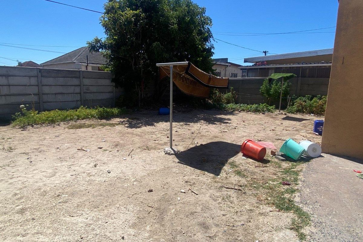 A rear outdoor space featuring a concrete boundary wall, sandy ground, and a metal washing line structure.