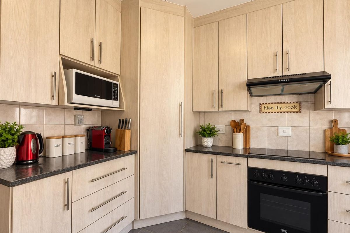 A well-maintained kitchen featuring light wood-grain cabinetry, dark laminate countertops, a built-in oven with hob, and a tiled backsplash.