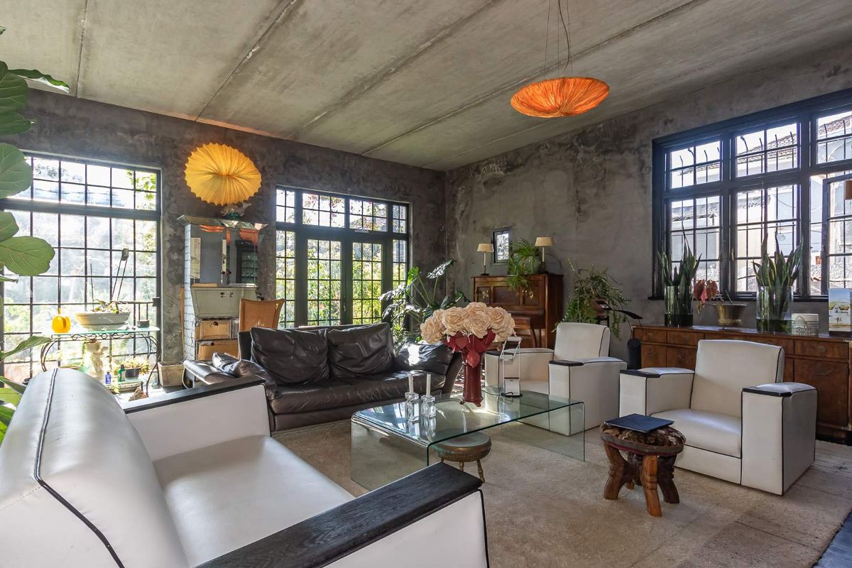 Spacious living room featuring industrial-style exposed concrete walls and ceilings, complemented by large steel-framed windows and doors that provide ample natural light.
