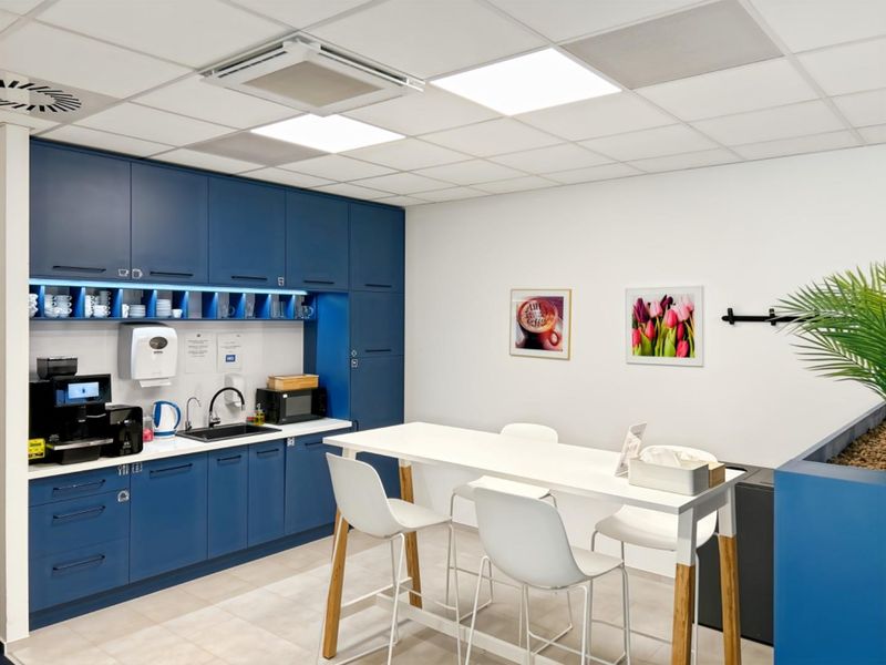 A modern office kitchenette featuring sleek blue cabinetry, integrated sink, and professional recessed lighting in a clean, well-maintained workspace environment.