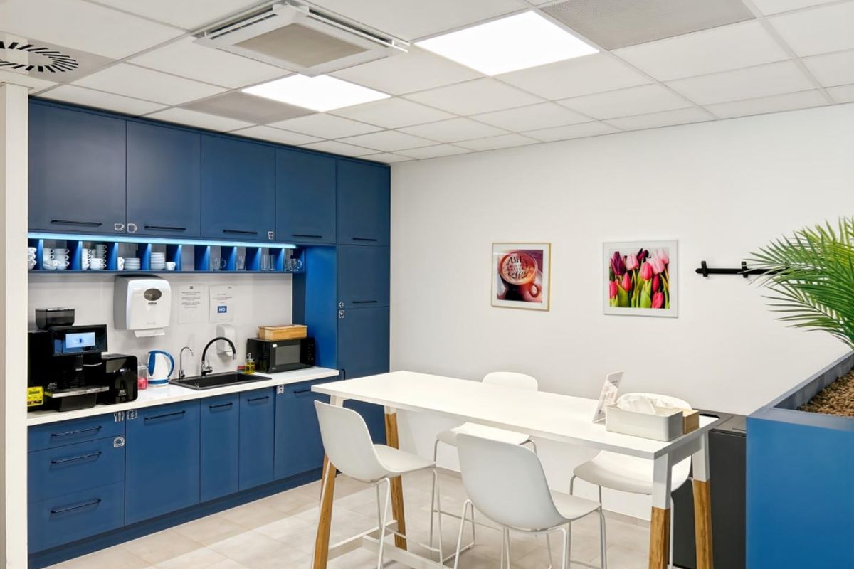 A modern office kitchenette featuring sleek blue cabinetry, integrated sink, and professional recessed lighting in a clean, well-maintained workspace environment.