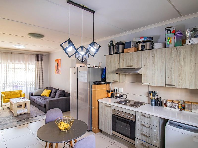 Open-plan living area featuring a functional kitchen with built-in cabinetry, electric hob, and oven, seamlessly flowing into a comfortable lounge space.