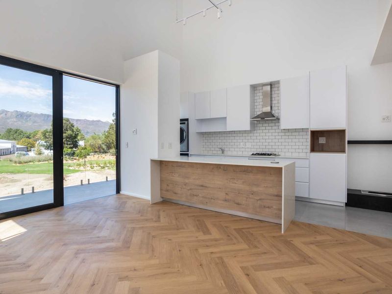 Modern open-plan living area featuring herringbone timber floors, a sleek kitchen with stone island, and large sliding doors opening to scenic mountain views.