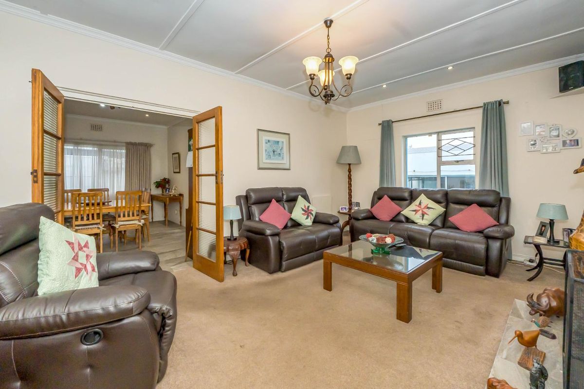 A comfortable living room featuring carpeted flooring, a classic chandelier, and double doors leading into an adjacent dining area.