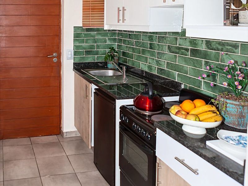 A functional kitchen featuring white and wood-tone cabinetry, dark granite countertops, a green subway tile backsplash, and a freestanding oven.