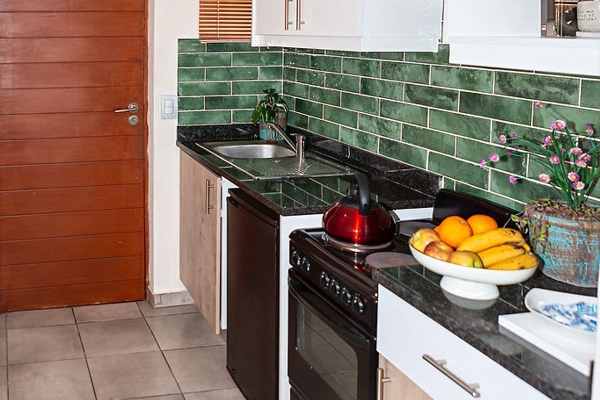 A functional kitchen featuring white and wood-tone cabinetry, dark granite countertops, a green subway tile backsplash, and a freestanding oven.