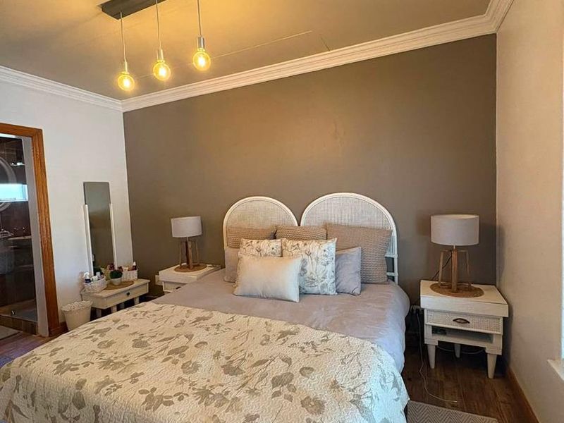 A well-maintained bedroom featuring hardwood flooring, crown molding, and a modern pendant light fixture, with an adjacent en-suite bathroom entrance.