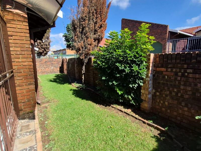 A private rear garden area featuring a brick boundary wall, lawn, and established greenery, accessible from the side of the townhouse.