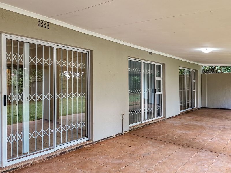 A spacious covered patio featuring tiled flooring and multiple sliding glass doors with security gates, providing seamless access to the interior living spaces.
