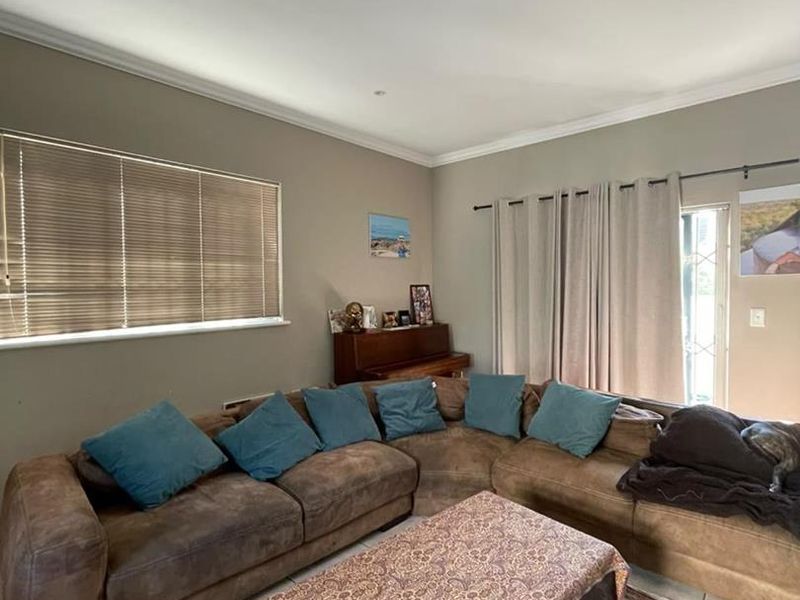 A comfortable living room featuring tiled flooring, recessed downlighting, crown molding, and natural light provided by a large window and sliding glass door.