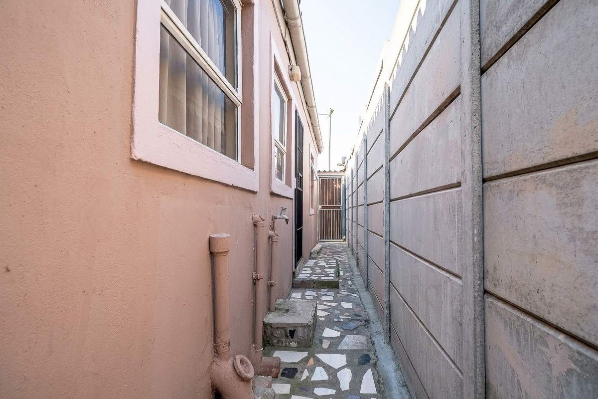 A narrow side passage featuring a paved walkway, external water tap, and a precast concrete boundary wall.