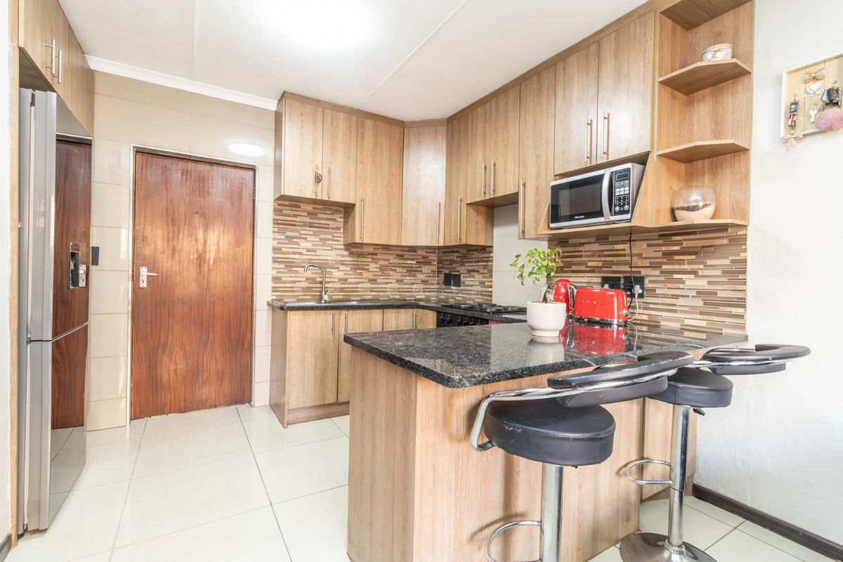 A functional kitchen featuring wood-look cabinetry, granite countertops, a mosaic tile backsplash, and a breakfast bar peninsula.