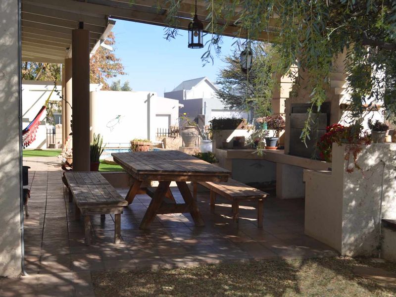 A covered outdoor patio area featuring a built-in braai, tiled flooring, and direct access to the garden and pool area.