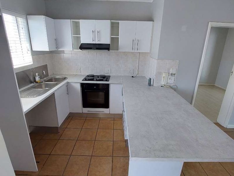 A functional kitchen featuring white cabinetry, laminate countertops, built-in oven and hob, tiled backsplash, and ceramic floor tiles.