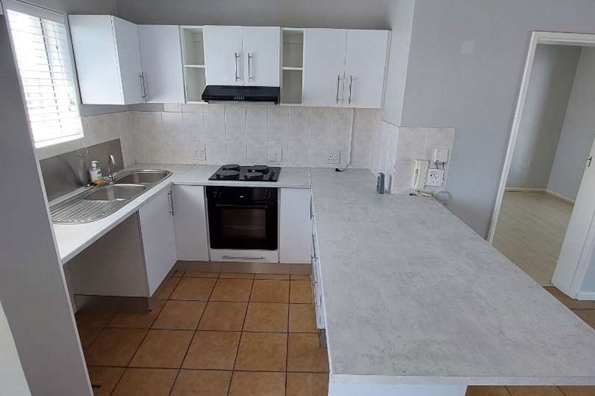 A functional kitchen featuring white cabinetry, laminate countertops, built-in oven and hob, tiled backsplash, and ceramic floor tiles.