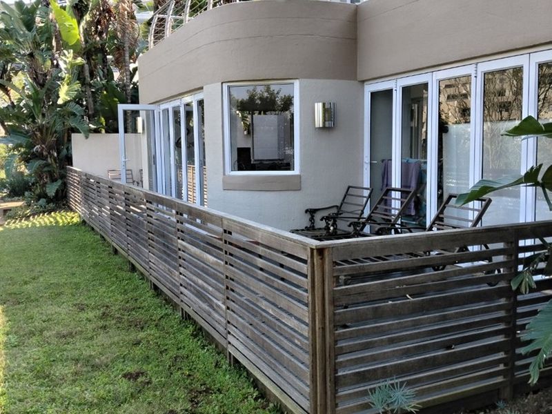 Rear exterior view of the apartment featuring a ground floor patio with timber slat fencing, folding glass doors, and an upper level balcony with balustrade.