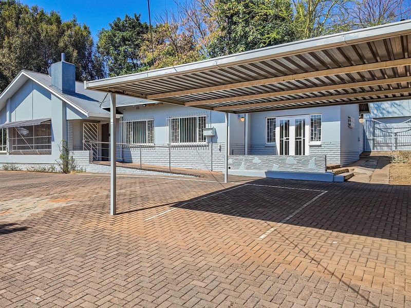 Front exterior view of the property featuring a large paved driveway, a covered carport, and accessible ramp entry with security bars on windows.