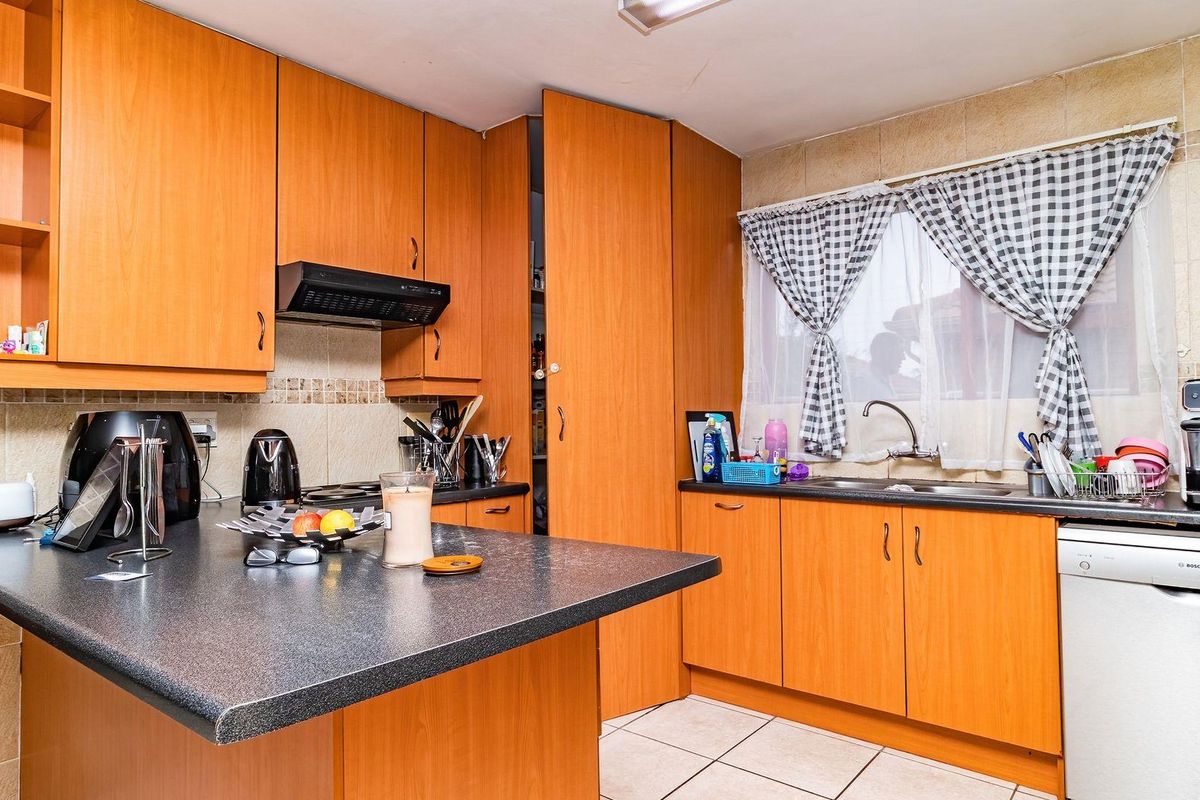 A functional kitchen featuring wood-look cabinetry, dark laminate countertops, a built-in extractor fan, and a double sink with tiled backsplash.