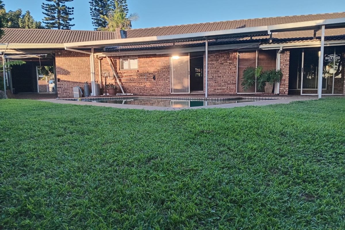 Rear view of a brick house featuring a swimming pool, covered patio area, and a well-maintained lawn.