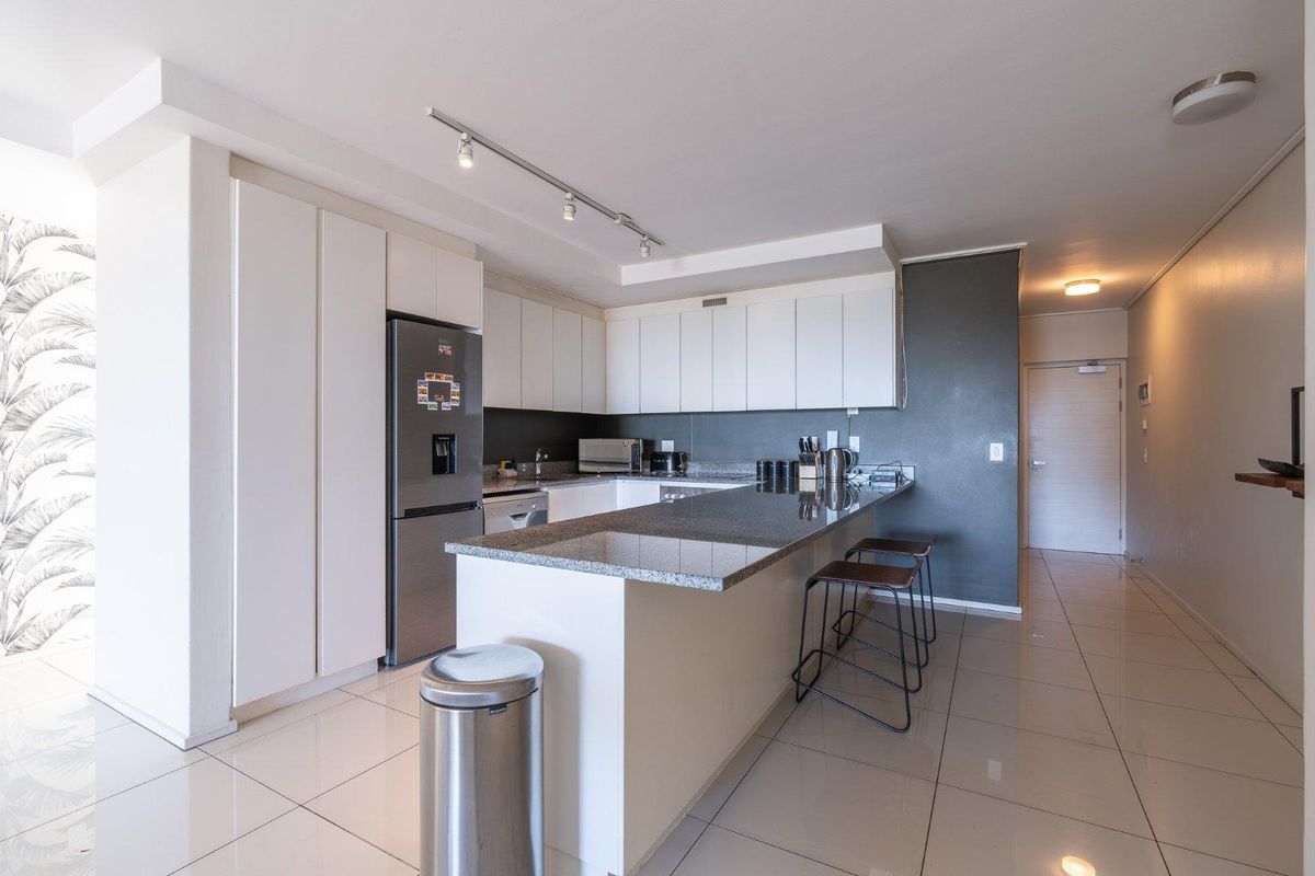 Modern kitchen featuring granite countertops, ample built-in cabinetry, a breakfast bar, and sleek tiled flooring, creating a functional and contemporary cooking space.
