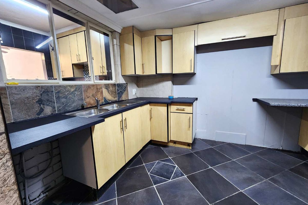 A functional kitchen featuring light wood-tone cabinetry, dark laminate countertops, a double stainless steel sink, and dark tiled flooring.