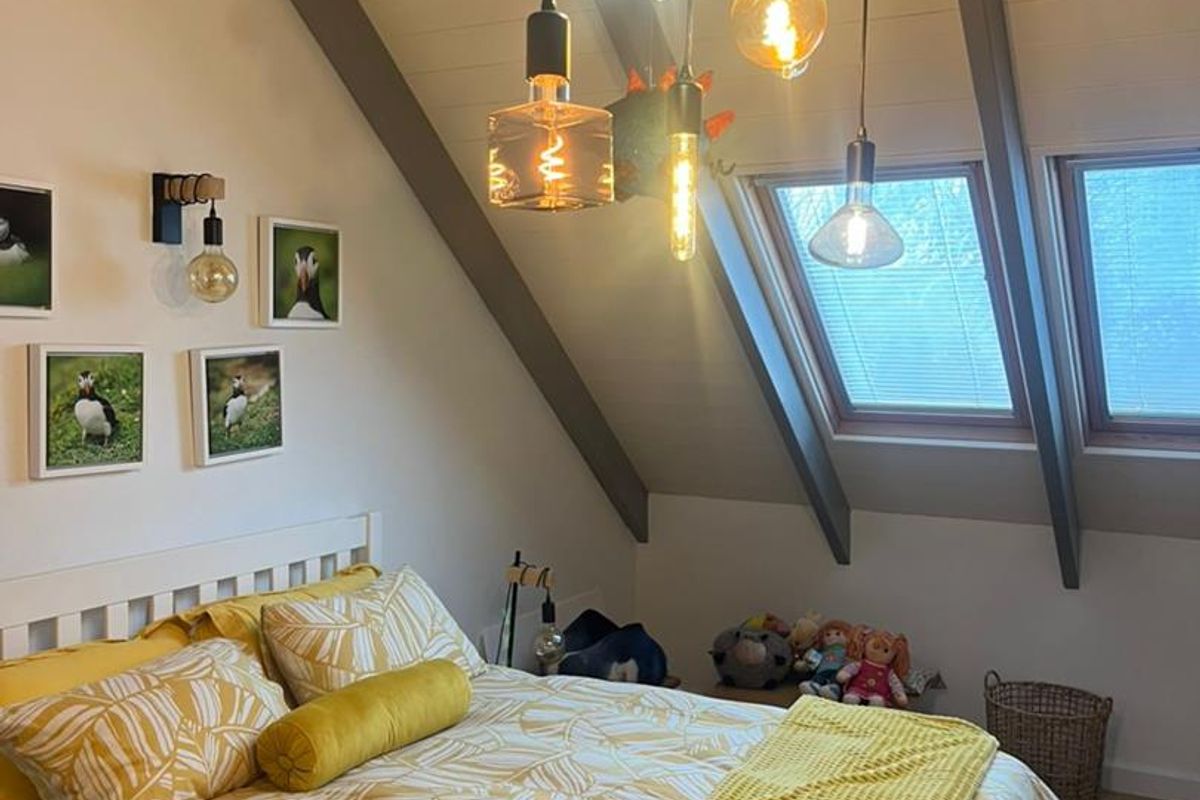 A cozy attic bedroom featuring exposed timber beams, skylight windows, and modern pendant lighting, creating a warm and inviting atmosphere.