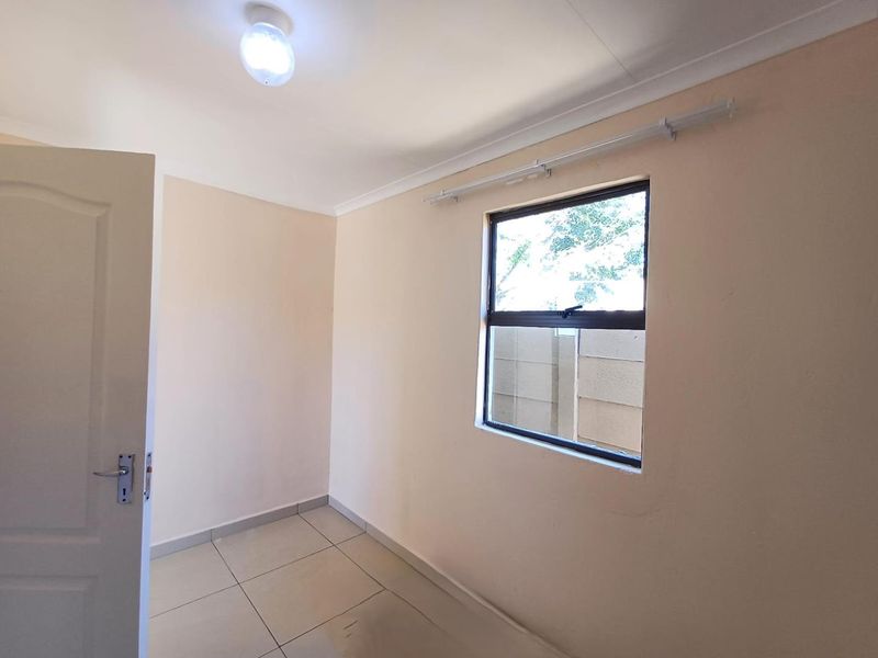 A clean, empty bedroom featuring neutral tiled flooring, cove cornicing, and a functional casement window with a curtain rail installed.