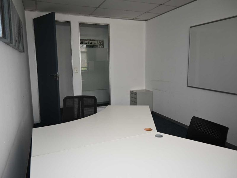 A functional office space featuring a suspended ceiling, glass partition, and wall-mounted whiteboard, suitable for a professional work environment.