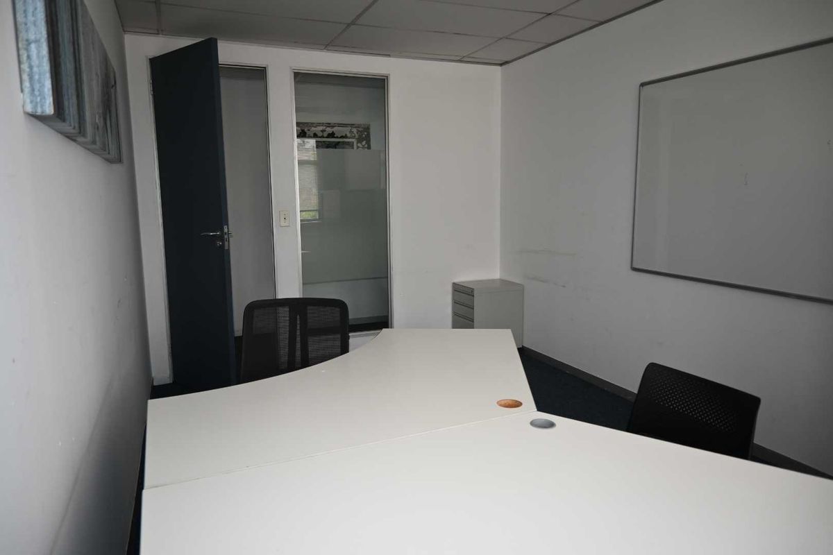 A functional office space featuring a suspended ceiling, glass partition, and wall-mounted whiteboard, suitable for a professional work environment.